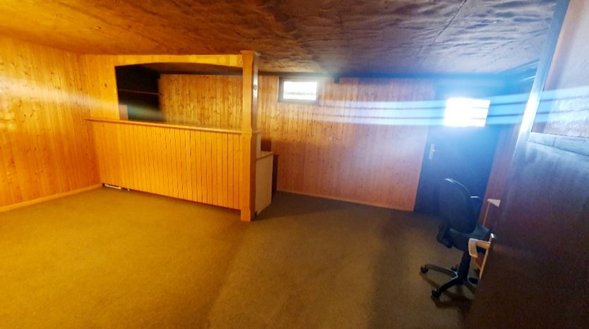 Heller Raum mit Holzverkleidung, Teppichboden, Fenster und einem Schreibtischstuhl in der Ecke.