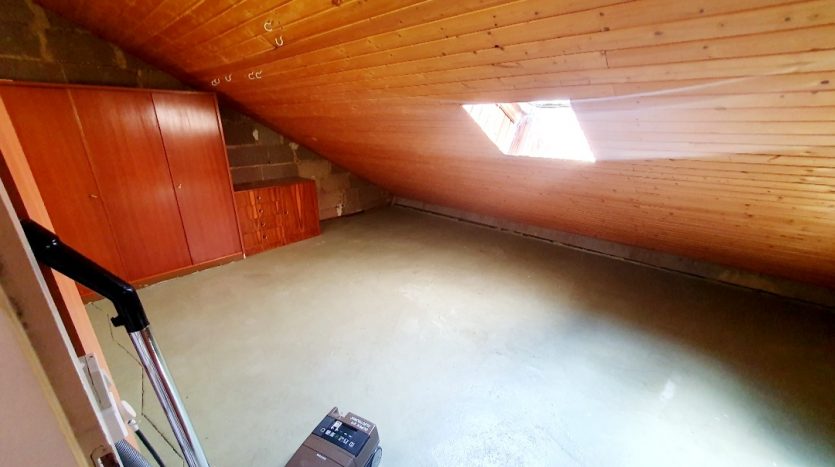 Dachboden mit schräger Holzdecke, Fensteröffnung und glattem Boden. Staubsauger steht im Raum.