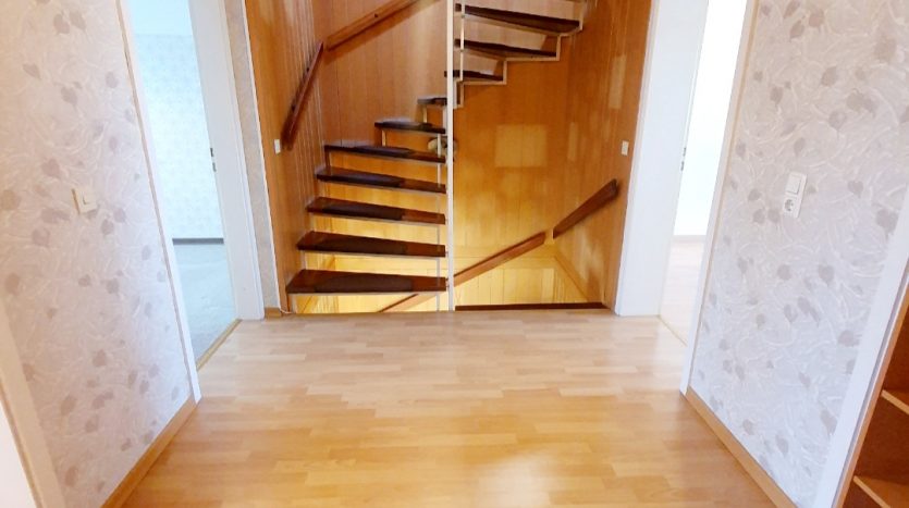 Heller Flur mit Holztreppe, Holzfußboden und dekorativen Tapeten, zwei Türen und Pendelleuchte.