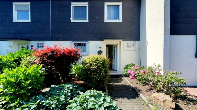 Eingangsbereich eines Hauses mit gepflegtem Garten, blühenden Pflanzen und einem Satellitenantenne auf dem Dach.