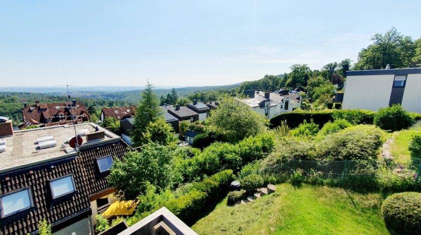 Blick auf ein Wohngebiet mit modernen Häusern, umgeben von Bäumen und Grünflächen, unter klarem Himmel.