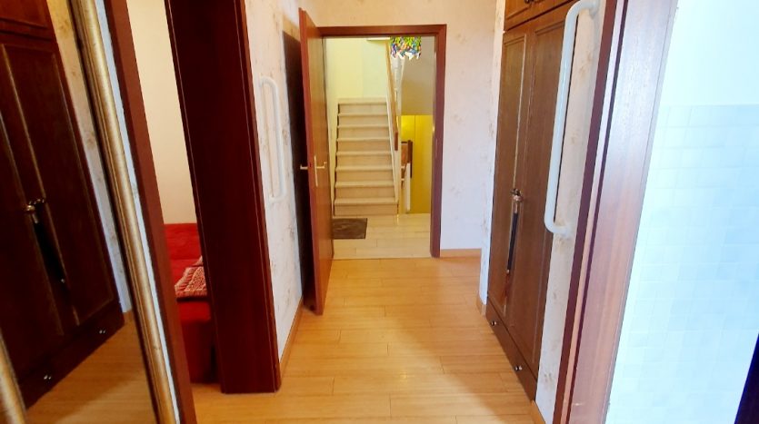 Heller Flur mit Holzverkleidung, Spiegeln, Treppe und Zugang zu einem Badezimmer. Holzfußboden und Deckenleuchte.