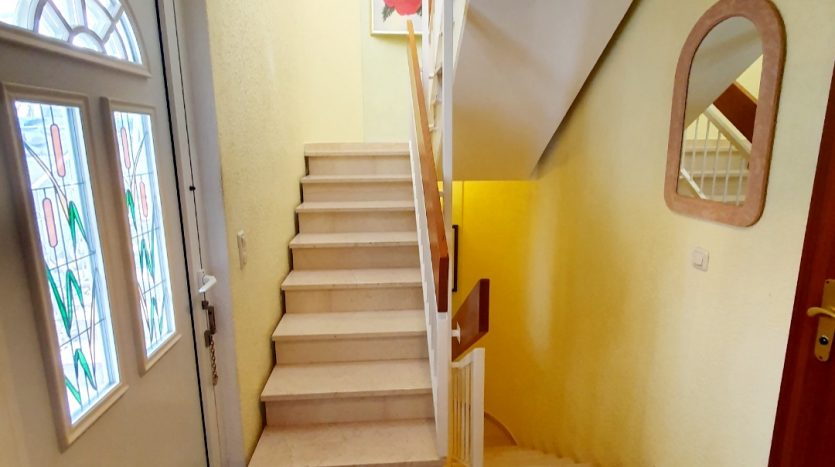 Heller Flur mit Treppe, buntem Glaslampenschirm und gemustertem Fußmatte. Wände in sanftem Gelb.