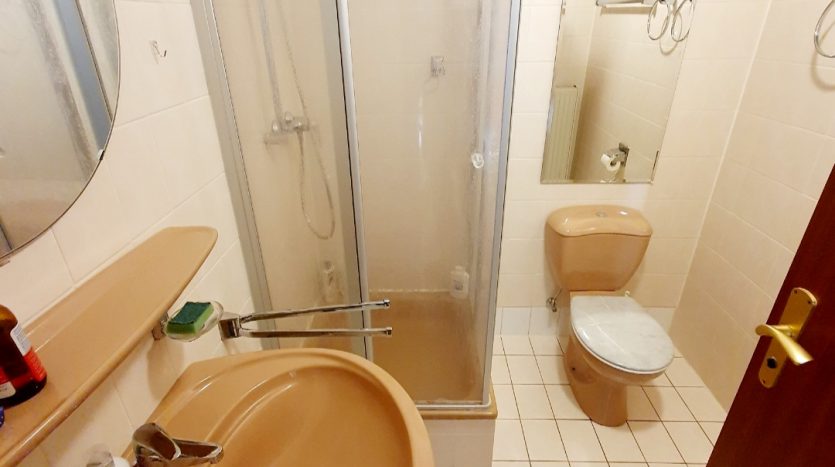 Kleines Badezimmer mit Dusche, Waschbecken und Toilette. Beige Fliesen und sanitäre Einrichtungen in neutralen Farben.
