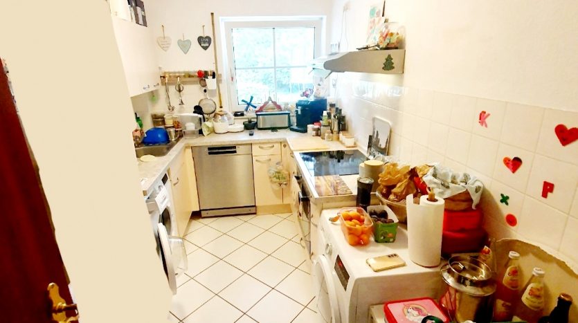 Küche mit weißen Wänden, Fenster, Waschmaschine, Geschirrspüler und vielen Küchenutensilien auf der Arbeitsfläche.