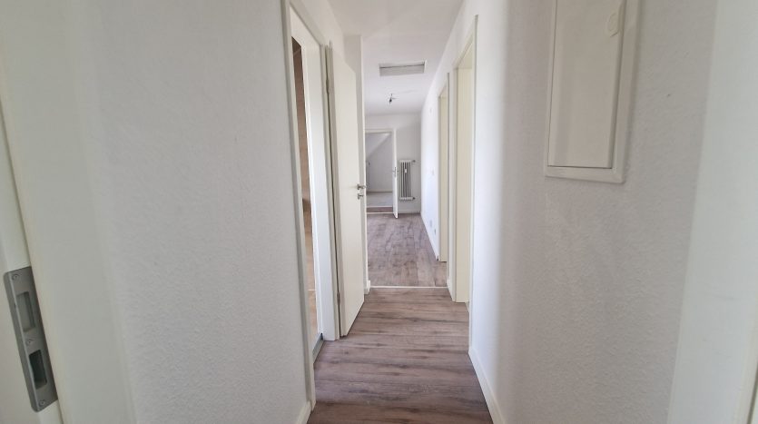 Heller Flur mit weißen Wänden, Holzboden und mehreren Türen, die zu weiteren Räumen führen.