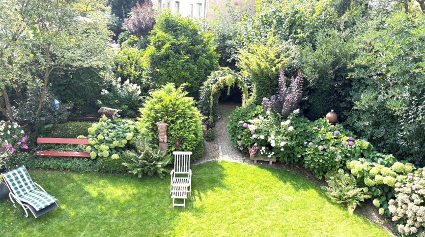 Blick auf einen üppigen Garten mit bunten Blumen, zwei Liegen und einer grünen Rasenfläche.