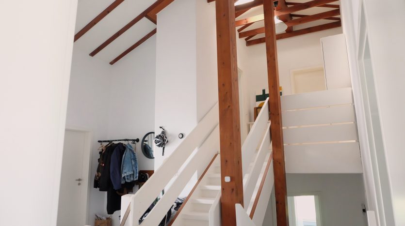 Heller Flur mit Holzdecke, Treppe und Garderobe. An der Wand hängen Jacken und ein Fahrradhelm.