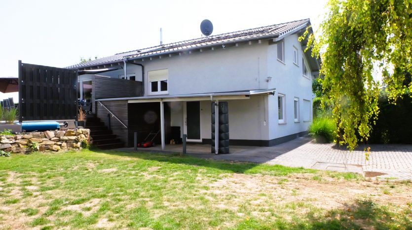 Zweifamilienhaus mit grauer Fassade, Terrasse, Garten und überdachtem Eingangsbereich. Sat-Anlage auf dem Dach.