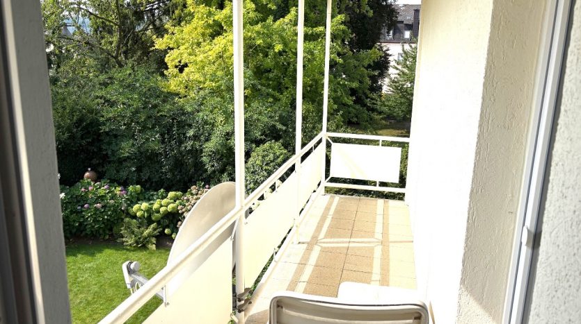 Balkon mit Blick auf üppige grüne Bäume und einen gepflegten Garten, ausgestattet mit einem Stuhl.