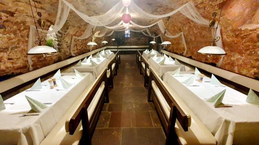 Gemütliches Restaurant mit langen Tischen, weißen Tischdecken und gefalteten Servietten in einer steinernen Höhle.
