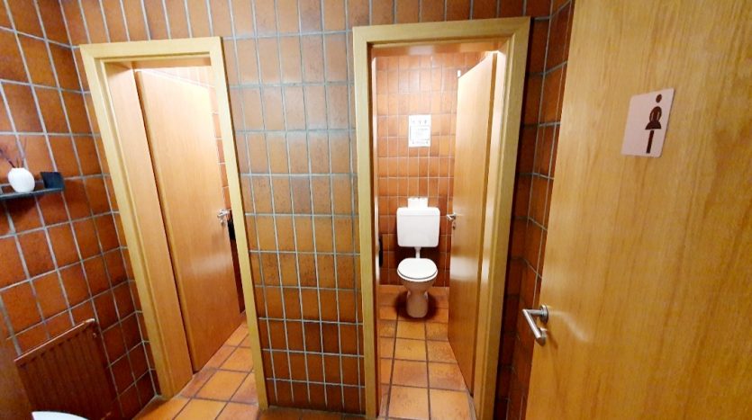 Zwei Toilettentüren in einem gefliesten Raum, eine mit männlichem, die andere mit weiblichem Symbol.